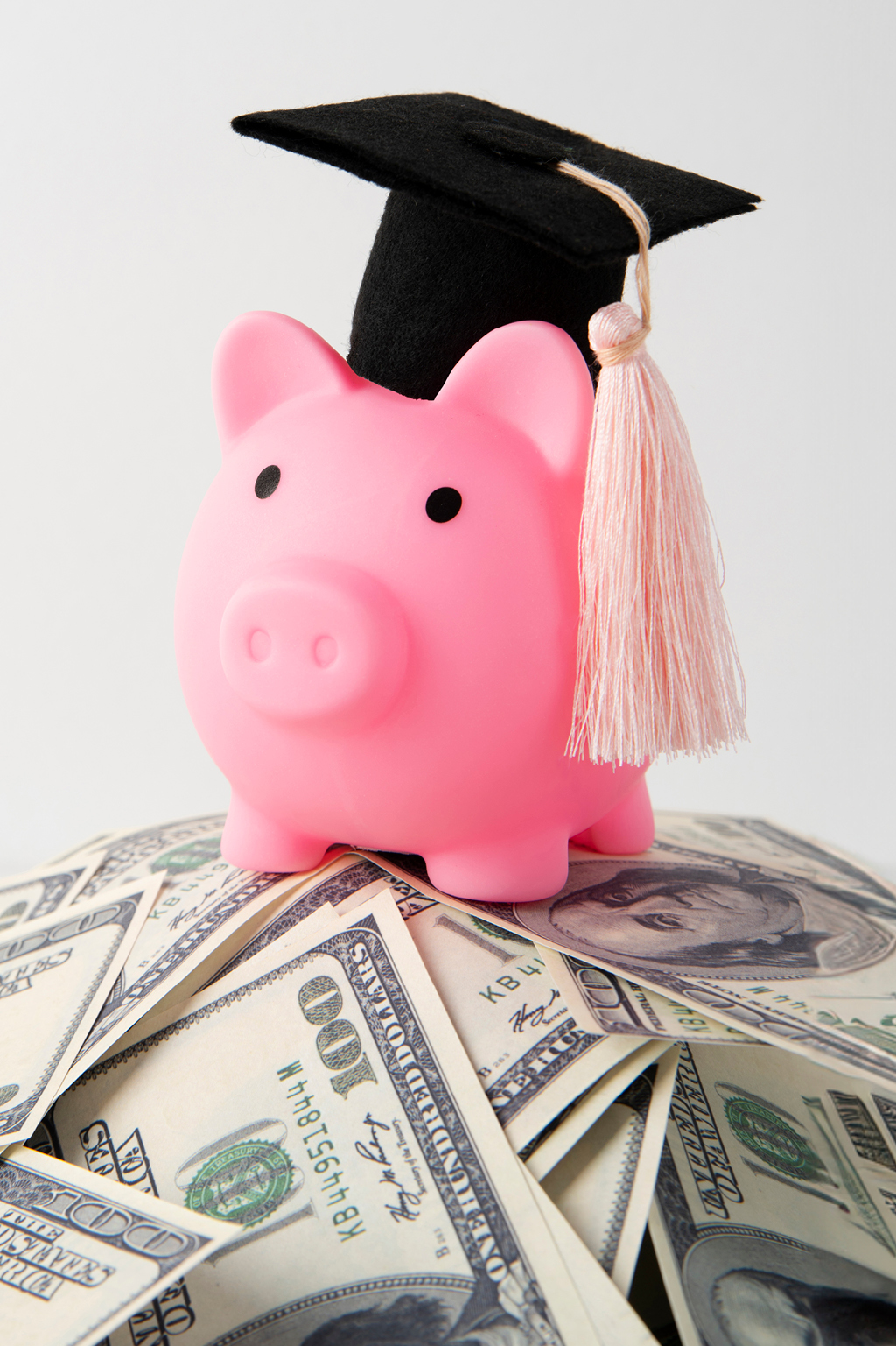 Pink toy pig wearing graduation cap on a stack of money
