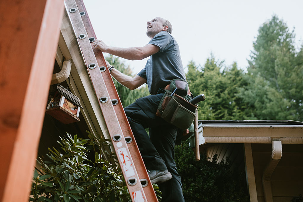 Man inspecting house on ladder outside