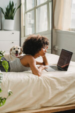 Woman at home laying on bed with dog on laptop