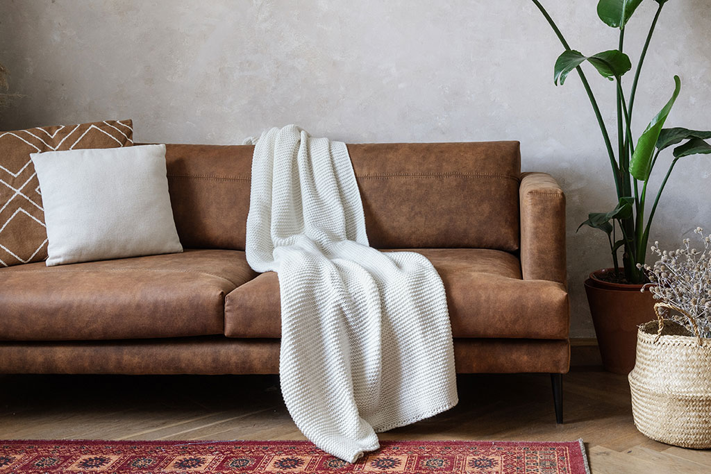 Brown leather couch with white throw and pillows