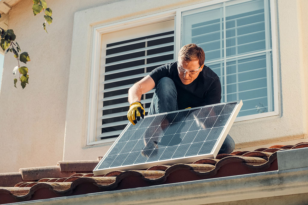 Man putting solar panel on roof of house