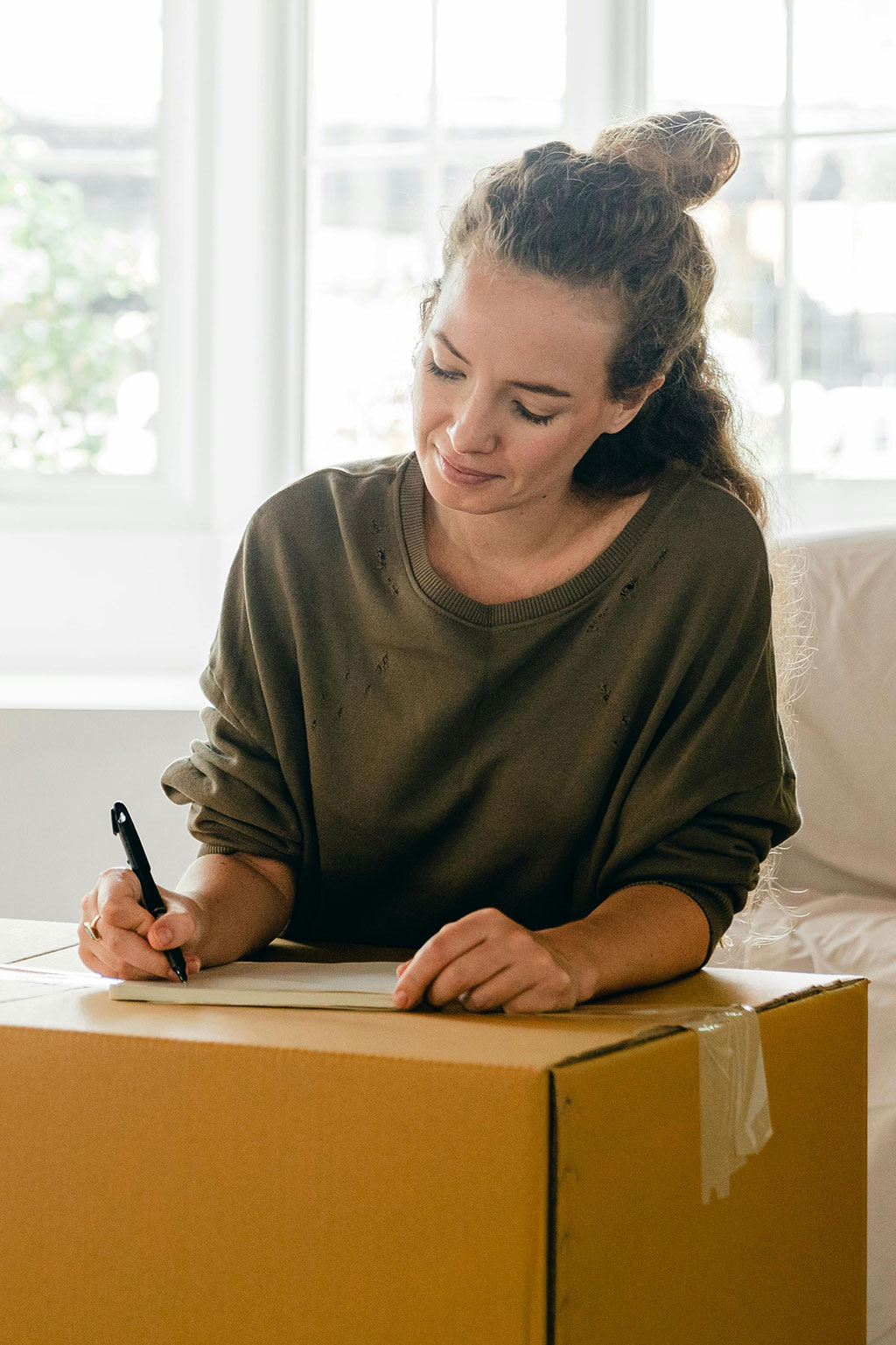 Woman writing on note pad on top of moving box